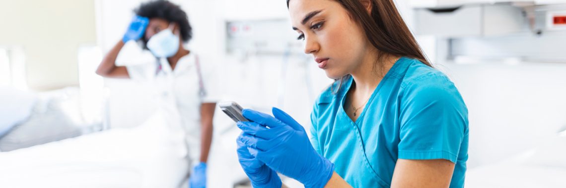 Young doctor womanand nurse taking a break during covid 19 epidemic. She is using her mobile phone and wearing her mask down