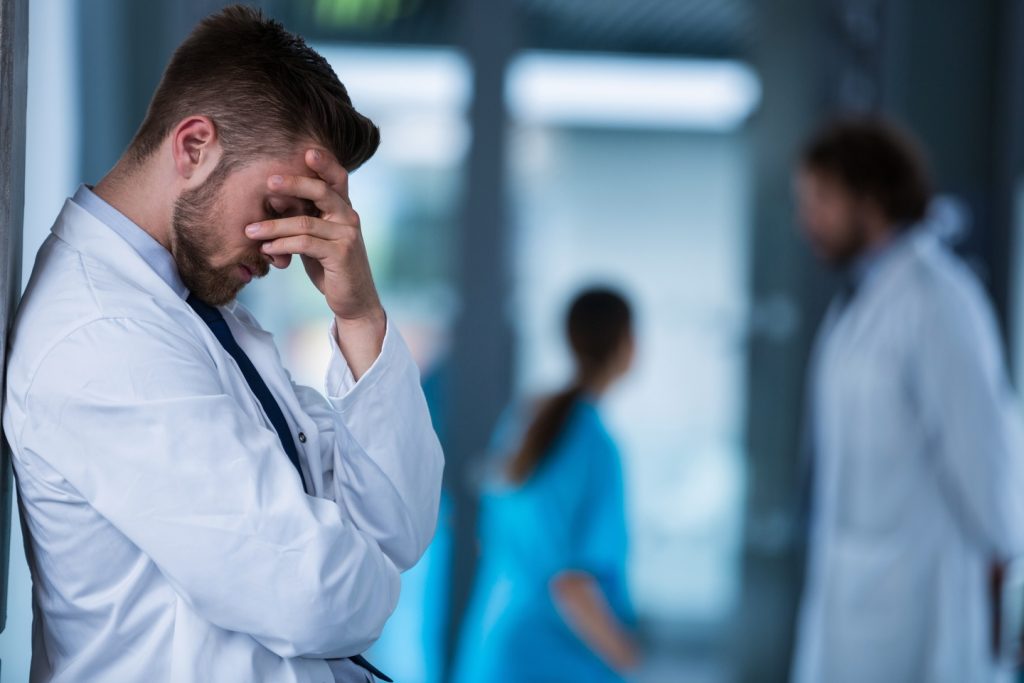 Stressed doctor standing against wall in hospital